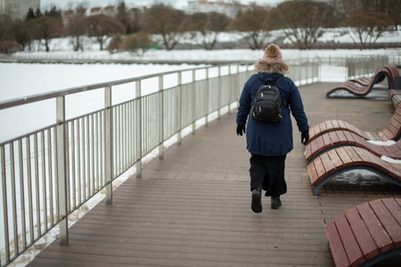Woman walks along promenade in winter. city park. Girl walks alone around the city.の写真素材