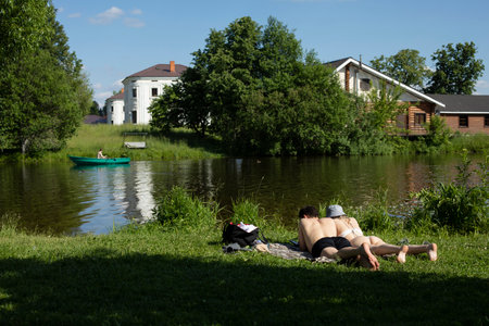 Beach on lake. Guy and girl lie on shore. Boat on water. countryside outside city. Rest in summer.の写真素材