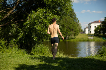 Guy goes to water in summer. Man swims in the lake. Rest in summer on shore. Details of life in countryside. Guy without clothes.の写真素材
