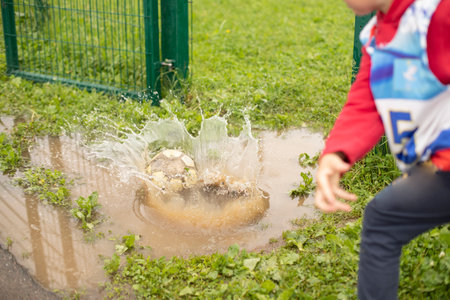 Child threw ball into puddle. hit water. splash game. Boy makes throw.の写真素材