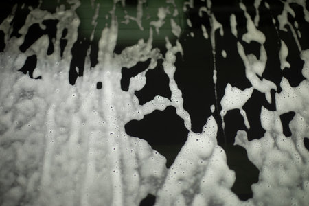 Soap foam on dark surface. Rinsing dirt off glass. Soap solution on car. Texture of white solution.の写真素材