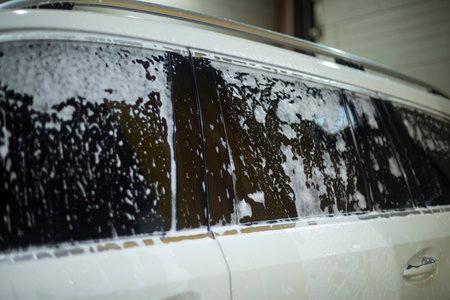White car at car wash. Soap foam in transport. Washing dirt from the body. Cleaning of transport.の写真素材