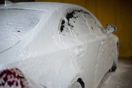 Machine in soap suds. Car wash in city. Cleaning car from dirt. White foam on transport.の写真素材