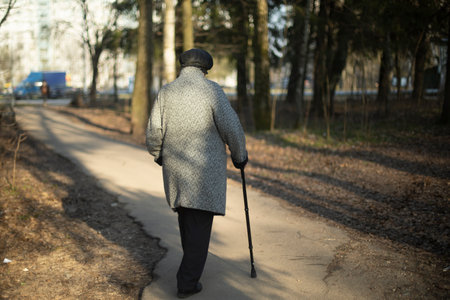 Pensioner with stick walks through park. Elderly person on road. Old woman walks around city. Path of life at end.の写真素材