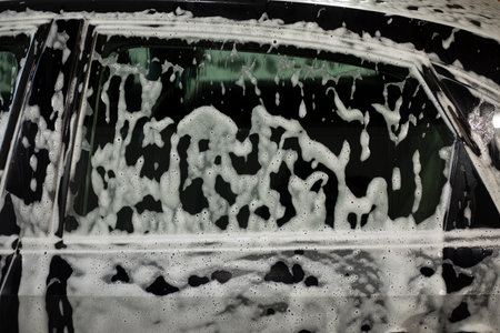 Car in soap foam. Car wash in the city. Foam on the body. Wet machine.の写真素材