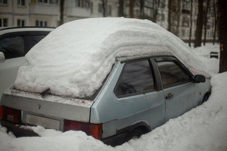 The car is in the parking lot in winter. The car is parked in the snow. Winter parking in the city. A lot of snow on the street and transport.の写真素材