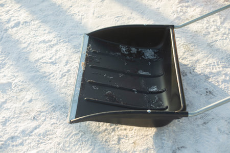 Black shovel for snow removal. Snow removal in yard. Large bucket made of black plastic. Details of restoring order in winter.の写真素材
