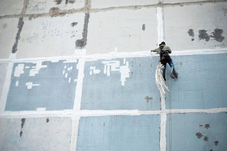 A climber paints a wall. The work of an industrial climber. Repair of the building wall. Applying paint to a house.の写真素材