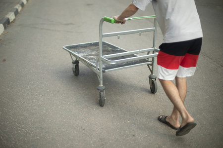 The guy pushes the cart. A man is carrying an empty cart. Loader on the road. Trolley for transporting small loads.の写真素材