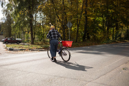A man crosses the road with a bicycle. Old man with bicycle walking across the highway. Elderly man in autumn. Pensioner in the city.の写真素材