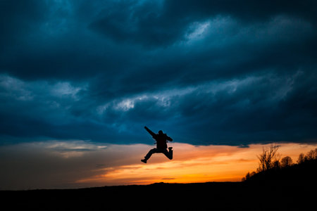 Man silhouette jumping against dramatic clouds background