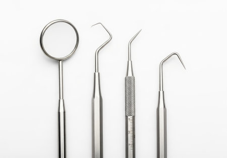 A set of four essential dental instruments is presented on a clean white surface. The tools include a dental mirror, explorer, and two types of scalers, all crucial for oral hygiene and check-ups.の素材