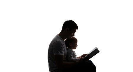 A person is depicted in silhouette, engrossed in reading a book. The stark contrast highlights their contemplative posture and focus.の素材