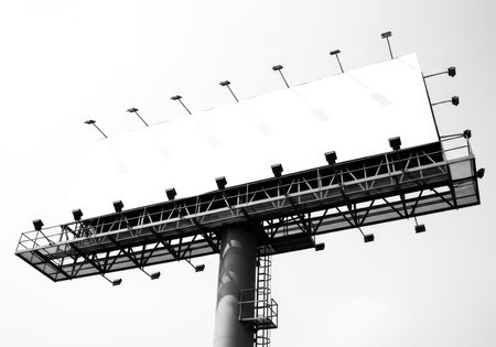 Monochrome, low-angle view of a large outdoor advertising billboard's robust metal structure and illuminating lights. Emphasizes urban infrastructure and commercial media.の素材