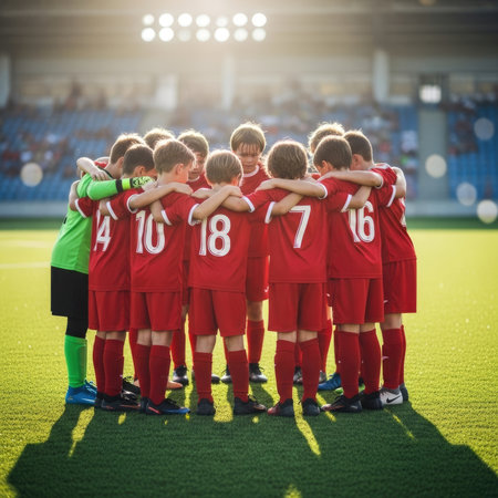 A group of young boys in red soccer jerseys form a huddle on a vibrant green football field, with stadium lights shining in the background, showing camaraderie and teamwork.の素材