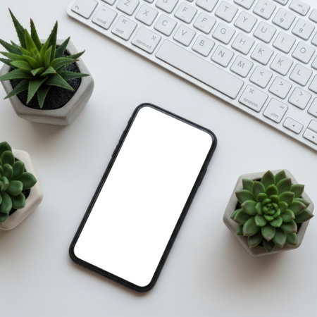 A minimalist workspace featuring a smartphone, keyboard, and three small succulent plants in white pots arranged on a clean, white surface.の素材