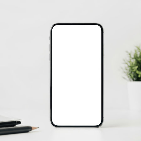 A sleek black smartphone stands upright on a clean, white desk. To the left of the phone, there are a few writing tools, including pens and pencils. On the right side, a small green plant adds a touch of nature to the minimalist setting.の素材