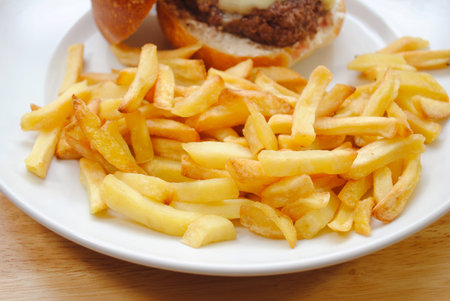 Crispy French Fries in a Plate with a Cheeseburger in the Backgroundの写真素材