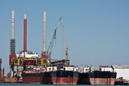 Large ships docked at an oil rig under construction with multiple cranes working.の写真素材