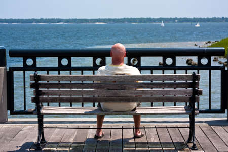 Man sitting on a bench at the ocean watching the sailboats.の写真素材