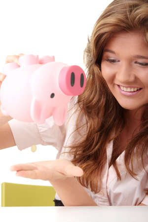 Young beautiful woman siting at the desk with piggy bank (money box), isolated on white backgroundの写真素材