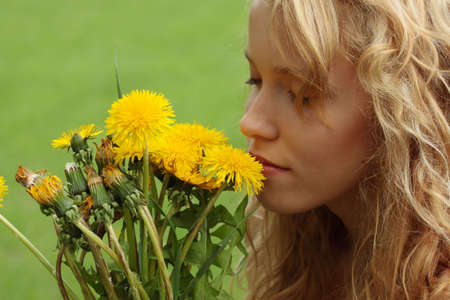 Beautiful young blond woman (girl) in a field enjoying the sun and smelling the yellow flowersの写真素材