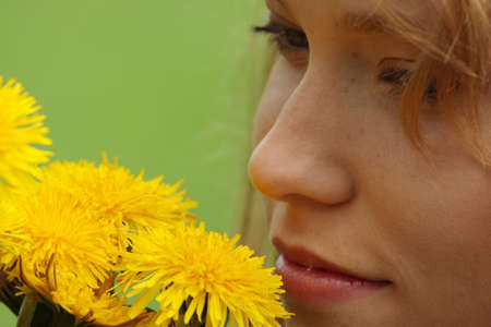 Beautiful young blond woman (girl) in a field enjoying the sun and smelling the yellow flowersの写真素材