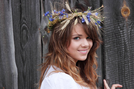 Beautiful young girl with grain wreath against old wood wallの写真素材