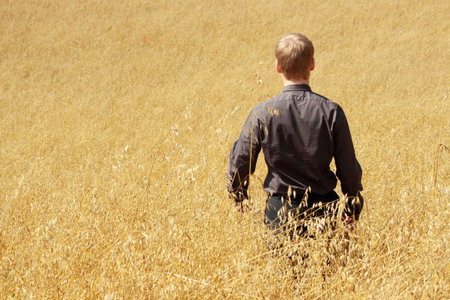 Young modern farmer in suit standing in field of oats

