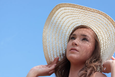A portrait of a beautiful woman in big summer hat against clear blue sky