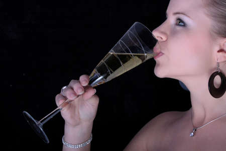 Beautiful blonde drinking a champagne from glass on black background.の写真素材