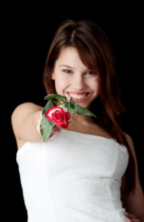Woman in an elegant white evening gown with rose in her hand isolated on blackの写真素材
