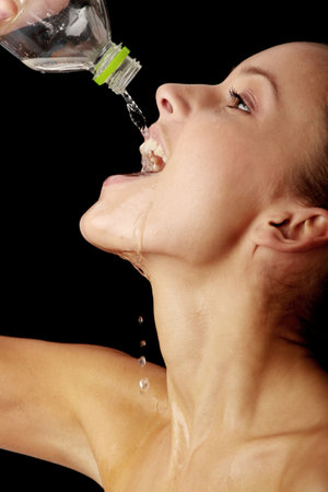 Young thirsty girl drinking water from a bottle isolated on black backgroundの写真素材