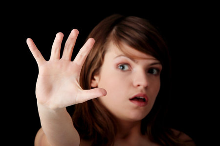 Young teen woman in act to defend herself from somebody striking out at her, isolated on black...