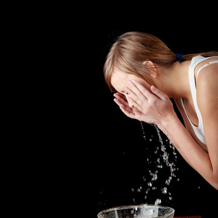 Teen girl washing her face with water, isolated on blackの写真素材