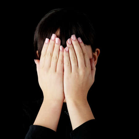 Young woman covering her eyes isolated on black backgroundの写真素材