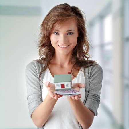 Beautiful young woman holding euros bills and house model over white - real estate loan conceptの写真素材