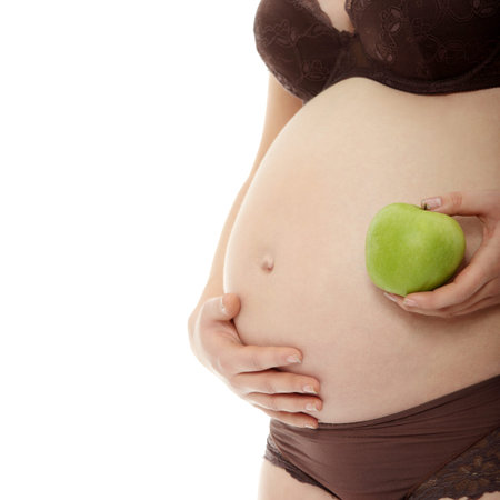 Belly of a pregnant woman with apple, isolated on white の写真素材