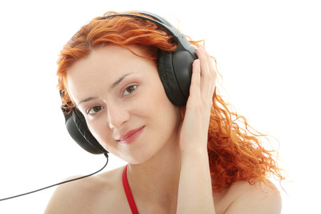 Attractive smiling redhead woman with headphones listening music, isolated on white