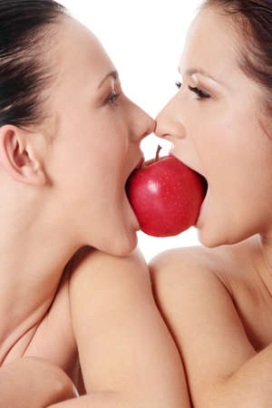 Two young woman biting an apple, isolated on white の写真素材