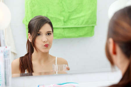 Young beautiful brunette woman using mouthwash at her bathroomの写真素材