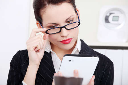 Beautiful caucasian businesswoman in glasses looking at the tablet in the office.の写真素材