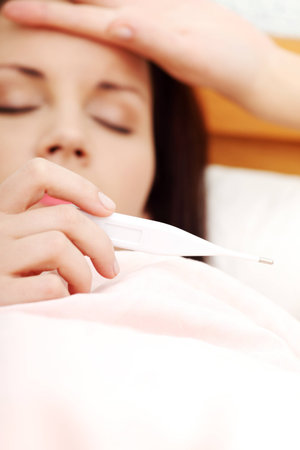 Face closeup of a beautiful woman resting in bed and having a cold, zoom in on the thermometer.