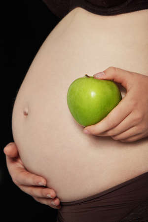 Belly of a pregnant woman with green apple, isolated on blackの写真素材