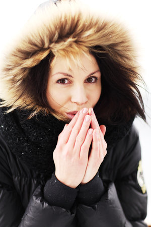 Beautiful woman trying to warm her hands with a breath in winter coat 