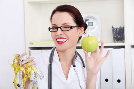 Woman dietician holding apple and  measuring tape and blinkingの写真素材