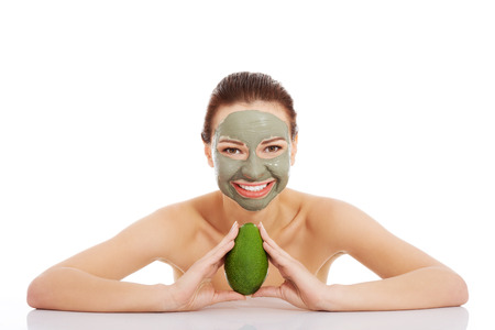 Beautiful woman with facial mask holding avocado. Isolated on white. の写真素材