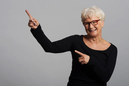 An old happy lady pointing on a copy space  On grey background 
