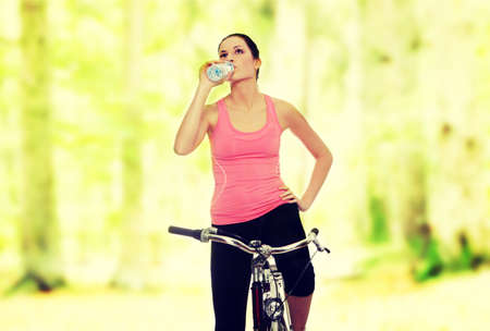 Attractive brunette woman with bike in forest drinking waterの写真素材