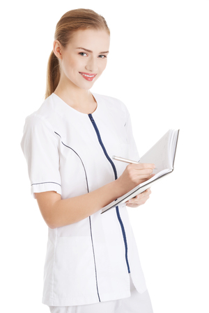 Beautiful caucasian nurse or doctor is writing in a notebook. Isolated on white.の写真素材